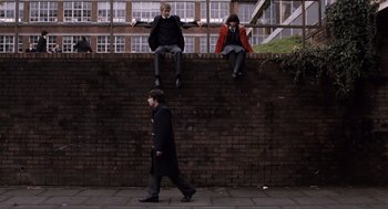 Movie still from “Submarine” (2010), directed by Richard Ayoade – A man walking down a sidewalk next to a brick wall; Wide shot, Low angle