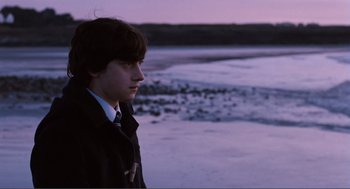 Movie still from “Submarine” (2010), directed by Richard Ayoade – A young man standing on the beach at dusk; Medium shot, Over the shoulder angle