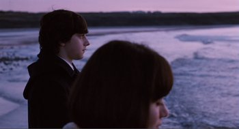 Movie still from “Submarine” (2010), directed by Richard Ayoade – A young man and a young woman standing next to a body of water; Medium shot, Over the shoulder angle