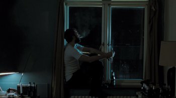 Movie still from “Submarino” (2010), directed by Thomas Vinterberg – A man sitting on a windowsill in front of a window at night; Medium shot, Low angle