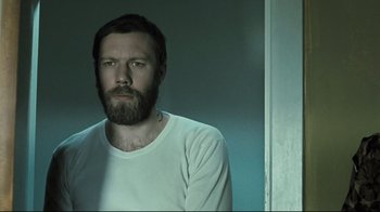 Movie still from “Submarino” (2010), directed by Thomas Vinterberg – A man with a long beard is standing in a room; Close Up shot, Low angle