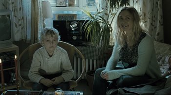 Movie still from “Submarino” (2010), directed by Thomas Vinterberg – A woman and a boy are sitting in a living room; Medium shot, Over the shoulder angle