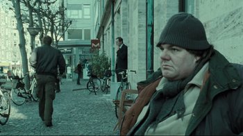 Movie still from “Submarino” (2010), directed by Thomas Vinterberg – A man in a winter coat and a hat on a street; Medium shot, Over the shoulder angle