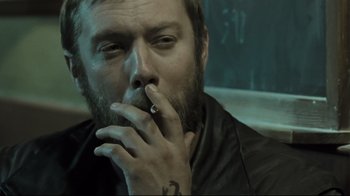 Movie still from “Submarino” (2010), directed by Thomas Vinterberg – A man with a beard smoking a cigarette in front of a chalkboard; Close Up shot, High angle