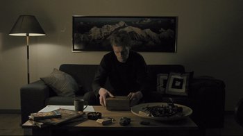 Movie still from “Submarino” (2010), directed by Thomas Vinterberg – A man sitting on a couch looking at an ipad; Wide shot, High angle