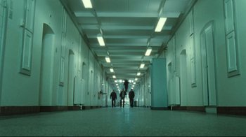 Movie still from “Submarino” (2010), directed by Thomas Vinterberg – Three people are walking down a hallway in a building; Extreme Wide shot, Low angle
