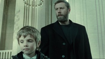 Movie still from “Submarino” (2010), directed by Thomas Vinterberg – A man and a boy standing next to each other in a room; Medium shot, Low angle