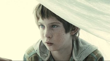 Movie still from “Submarino” (2010), directed by Thomas Vinterberg – A young boy with blue eyes is under an umbrella; Close Up shot, Low angle