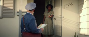 Movie still from “Suburbicon” (2017), directed by George Clooney – A woman in a dress and a man in a blue suit are standing in front of a door; Medium shot, Low angle
