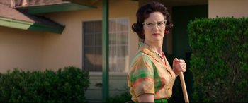 Movie still from “Suburbicon” (2017), directed by George Clooney – An older woman wearing glasses standing in front of a house; Medium shot, Low angle