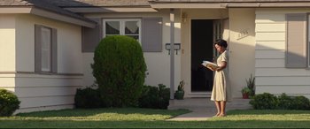 Movie still from “Suburbicon” (2017), directed by George Clooney – A woman standing in front of a house holding a book; Wide shot, Low angle