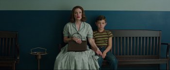 Movie still from “Suburbicon” (2017), directed by George Clooney – A woman sitting on a bench next to a young boy; Medium shot, Low angle