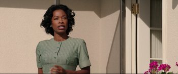 Movie still from “Suburbicon” (2017), directed by George Clooney – A woman in a green dress is standing in front of a wall; Medium shot, Low angle