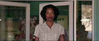 Movie still from “Suburbicon” (2017), directed by George Clooney – A woman in a white shirt is standing in front of a green wall; Medium shot, Low angle