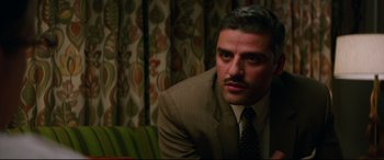 Movie still from “Suburbicon” (2017), directed by George Clooney – A man in a suit and tie sitting in front of a curtain; Close Up shot, Over the shoulder angle