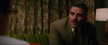 Movie still from “Suburbicon” (2017), directed by George Clooney – A man wearing a suit and tie sitting on a couch; Close Up shot, Over the shoulder angle