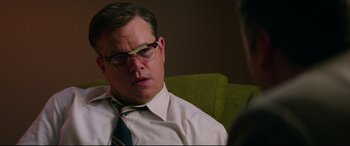 Movie still from “Suburbicon” (2017), directed by George Clooney – A man wearing a tie and glasses sitting on a green chair; Close Up shot, Over the shoulder angle