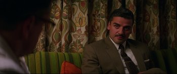 Movie still from “Suburbicon” (2017), directed by George Clooney – A man in a suit and tie sitting on top of a couch; Close Up shot, Over the shoulder angle