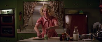 Movie still from “Suburbicon” (2017), directed by George Clooney – A woman in a pink dress is cutting a sandwich; Medium shot, Low angle