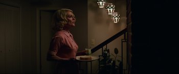 Movie still from “Suburbicon” (2017), directed by George Clooney – A woman holding a tray with a cake on top of it; Medium shot, Low angle