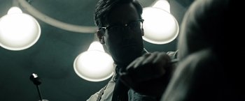 Movie still from “Sucker Punch” (2011), directed by Zack Snyder – A man wearing glasses and a tie in the dark; Close Up shot, Low angle