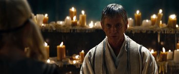 Movie still from “Sucker Punch” (2011), directed by Zack Snyder – An older man standing in front of candles in a room; Close Up shot, Over the shoulder angle