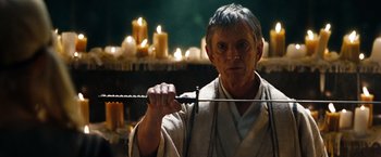 Movie still from “Sucker Punch” (2011), directed by Zack Snyder – An older man holding a sword in front of candles; Close Up shot, Low angle