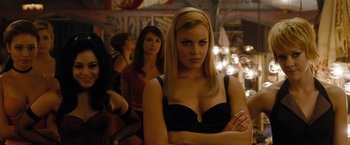 Movie still from “Sucker Punch” (2011), directed by Zack Snyder – A woman in a black top is standing in front of two other women; Close Up shot, Over the shoulder angle