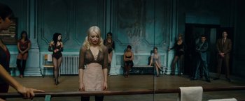 Movie still from “Sucker Punch” (2011), directed by Zack Snyder – A group of people sitting in front of a mirror on a stage; Wide shot, High angle