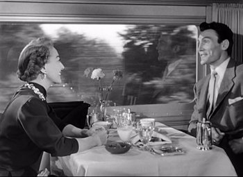 Movie still from “Sudden Fear” (1952), directed by David Miller – A man and a woman sitting at a dinner table in front of a train window; Medium shot, Over the shoulder angle
