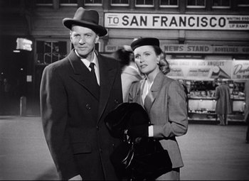 Movie still from “Sudden Fear” (1952), directed by David Miller – A man and a woman standing next to each other in front of a building; Medium shot, Low angle
