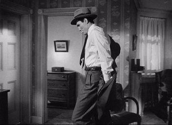 Movie still from “Sudden Fear” (1952), directed by David Miller – A black and white photo of a man wearing a hat and a tie; Medium shot, Low angle