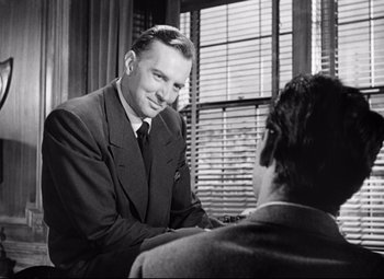Movie still from “Sudden Fear” (1952), directed by David Miller – A man sitting at a table talking to another man in a suit; Medium shot, Over the shoulder angle