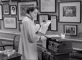 Movie still from “Sudden Fear” (1952), directed by David Miller – A woman is standing in front of a printer and looking at a paper; Medium shot, High angle