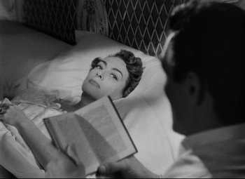 Movie still from “Sudden Fear” (1952), directed by David Miller – A woman laying in a bed reading a book to a man; Close Up shot, High angle