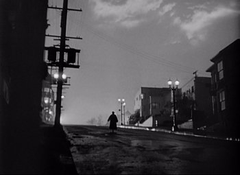 Movie still from “Sudden Fear” (1952), directed by David Miller – A man riding a skateboard down the middle of a street; Extreme Wide shot, Low angle