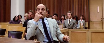 Movie still from “Sudden Impact” (1983), directed by Clint Eastwood – A man sitting in front of a group of people in a court room; Medium shot, Low angle