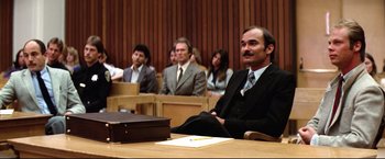 Movie still from “Sudden Impact” (1983), directed by Clint Eastwood – A man sitting in front of a group of people in a courtroom; Medium shot, Low angle