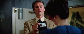 Movie still from “Sudden Impact” (1983), directed by Clint Eastwood – A man in a tan suit holding up a cell phone; Close Up shot, Over the shoulder angle