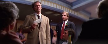 Movie still from “Sudden Impact” (1983), directed by Clint Eastwood – A group of men in suits and ties standing in a room; Medium shot, Over the shoulder angle