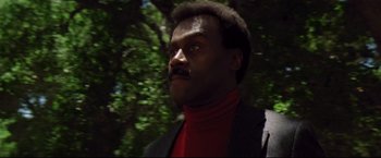 Movie still from “Sudden Impact” (1983), directed by Clint Eastwood – A man in a suit and a red shirt is in the woods; Close Up shot, Low angle