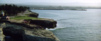 Movie still from “Sudden Impact” (1983), directed by Clint Eastwood – A body of water near a cliff with a person standing on it; Extreme Wide shot, High angle