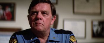 Movie still from “Sudden Impact” (1983), directed by Clint Eastwood – A man in a police uniform looking to his left; Close Up shot, Over the shoulder angle