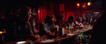 Movie still from “Sudden Impact” (1983), directed by Clint Eastwood – A group of people sitting at a long wooden table; Wide shot, Over the shoulder angle