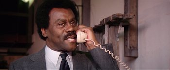 Movie still from “Sudden Impact” (1983), directed by Clint Eastwood – A man talking on a phone while wearing a suit and tie; Close Up shot, Low angle