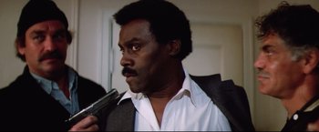 Movie still from “Sudden Impact” (1983), directed by Clint Eastwood – A man holding a gun while wearing a suit; Close Up shot, Low angle