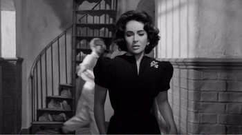 Movie still from “Suddenly, Last Summer” (1959), directed by Joseph L. Mankiewicz – A woman in a black dress standing in front of a staircase; Medium shot, Over the shoulder angle