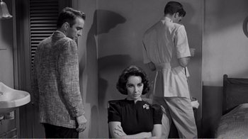 Movie still from “Suddenly, Last Summer” (1959), directed by Joseph L. Mankiewicz – A woman sitting in front of two men in front of a wall; Medium shot, Over the shoulder angle