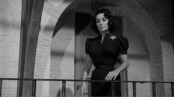 Movie still from “Suddenly, Last Summer” (1959), directed by Joseph L. Mankiewicz – A woman in a black dress standing next to a railing in front of a brick building; Medium shot, Low angle