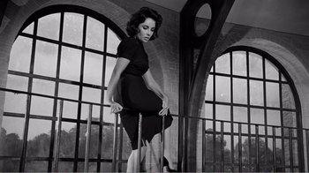 Movie still from “Suddenly, Last Summer” (1959), directed by Joseph L. Mankiewicz – A black and white photo of a woman standing on a railing in front of windows; Medium shot, Low angle